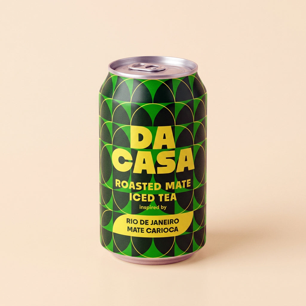 A single aluminum can of DA CASA Roasted Mate Iced Tea, featuring a green and black geometric pattern with bold yellow lettering, set against a solid beige background.
